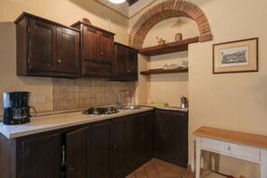 Une cuisine avec des meubles de couleur bois foncé, un pare-feu en carreaux, une machine à café et une arche en briques.
