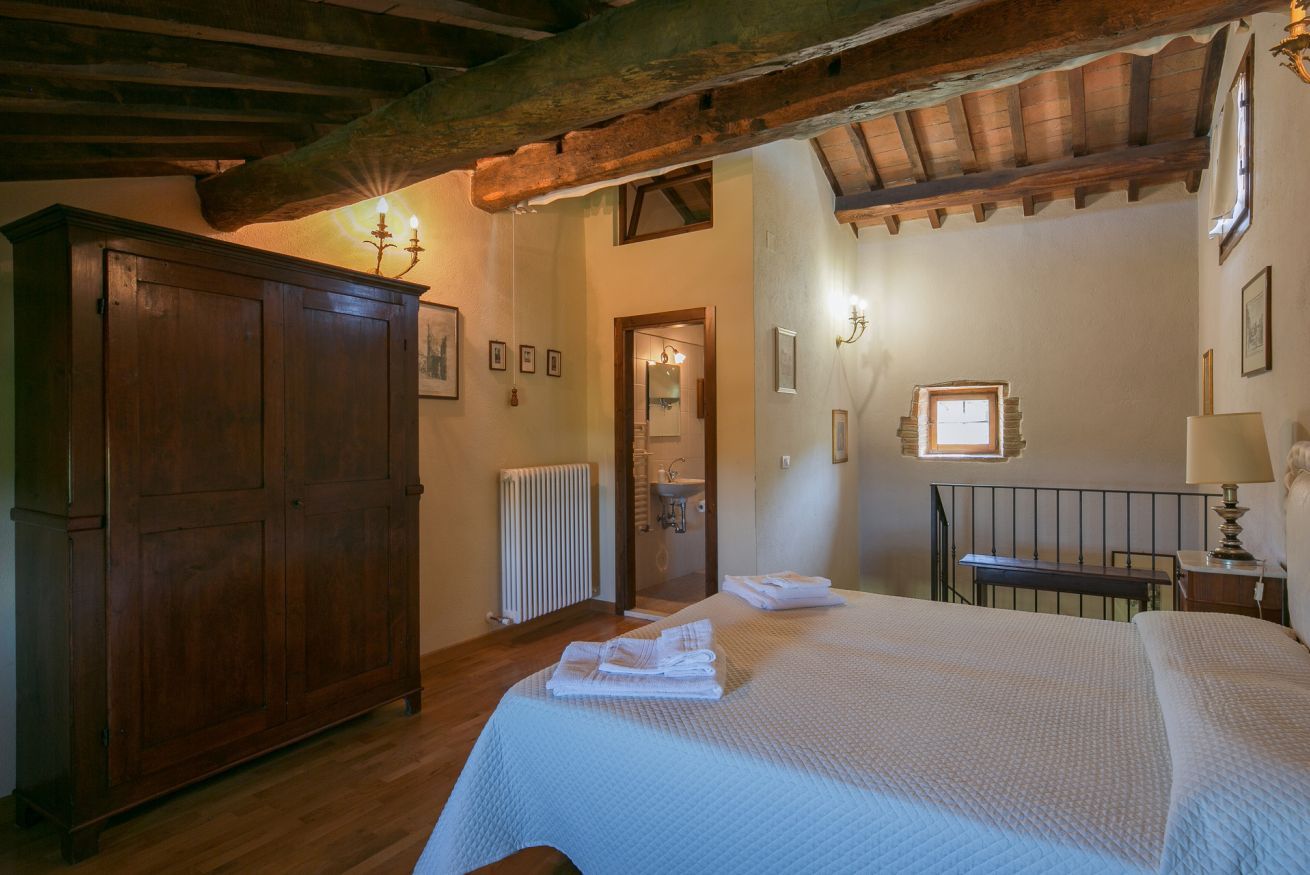 A bedroom with a large wooden wardrobe, a bed with neatly folded white towels, and a rustic ceiling.