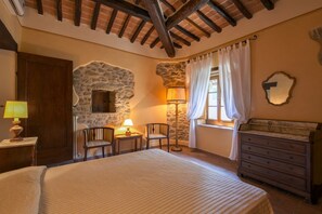 Een slaapkamer met een bed, een dressoir, een stenen muur, een lamp en een stoel.