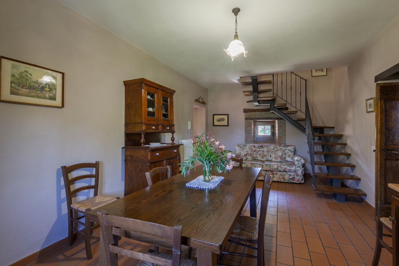 A dining area with a wooden table, chairs, a cabinet, and a staircase leading to another level.