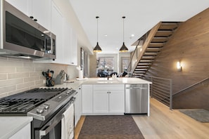 A modern kitchen with stainless steel appliances, a central island, and a wooden staircase.