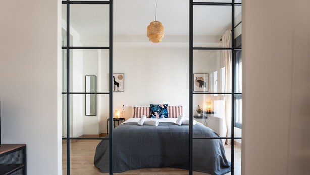 Une chambre à coucher moderne avec un grand lit, une table de chevet avec une lampe et un miroir fixé au mur.