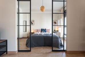 Un dormitorio moderno con una cama grande, una mesita de noche con lámpara y un espejo en la pared.