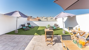 Une terrasse sur le toit avec deux chaises longues, une petite table et un pot de fleurs.