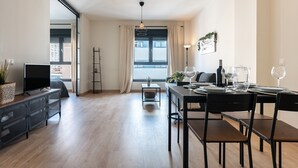 Un salon moderne doté d’un téléviseur à écran plat, d’un porte-manteau et d’un coin repas avec une table dressée pour deux personnes.