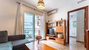 Un salon comprenant un canapé, une table basse en bois, un meuble pour la télévision avec un téléviseur à écran plat et une plante en pot.