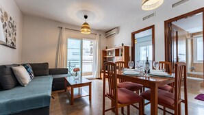 Un salon moderne avec un canapé, une table à manger pour quatre personnes et un grand miroir.