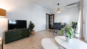 Un salon moderne avec un téléviseur à écran plat, un meuble vert, une table à manger avec des chaises et une grande fenêtre avec des rideaux.