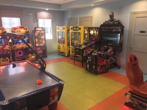 A room with arcade games, a pool table, and a large screen displaying a movie. - Nice house in the best resort in Orlando (Four Corners)