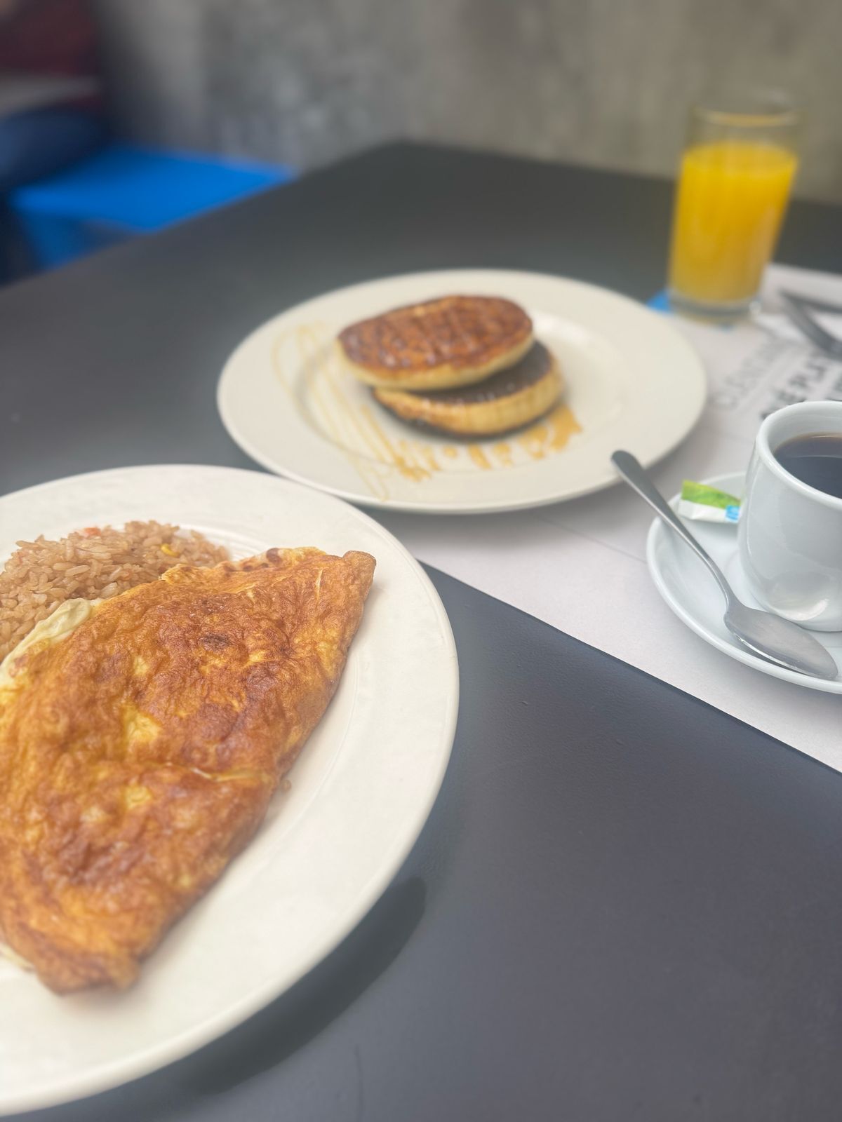 A breakfast setting with a plate of pancakes, a plate of fried rice, and a cup of coffee with a spoon.