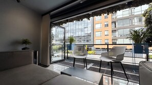 Une chambre moderne avec un balcon, un canapé, deux fauteuils et une vue sur le paysage urbain.