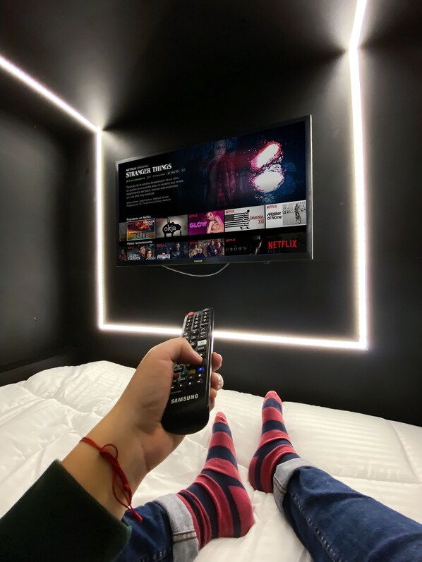 Une personne tenant une télécommande devant un téléviseur fixé au mur, qui affiche l’interface de Netflix.