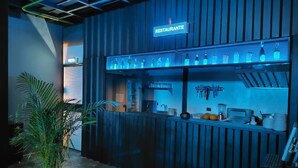 A modern bar area with a neon sign indicating a restaurant, shelves with bottles, and bar tools. - Hostal Joy Calle 85 (Bogotá)