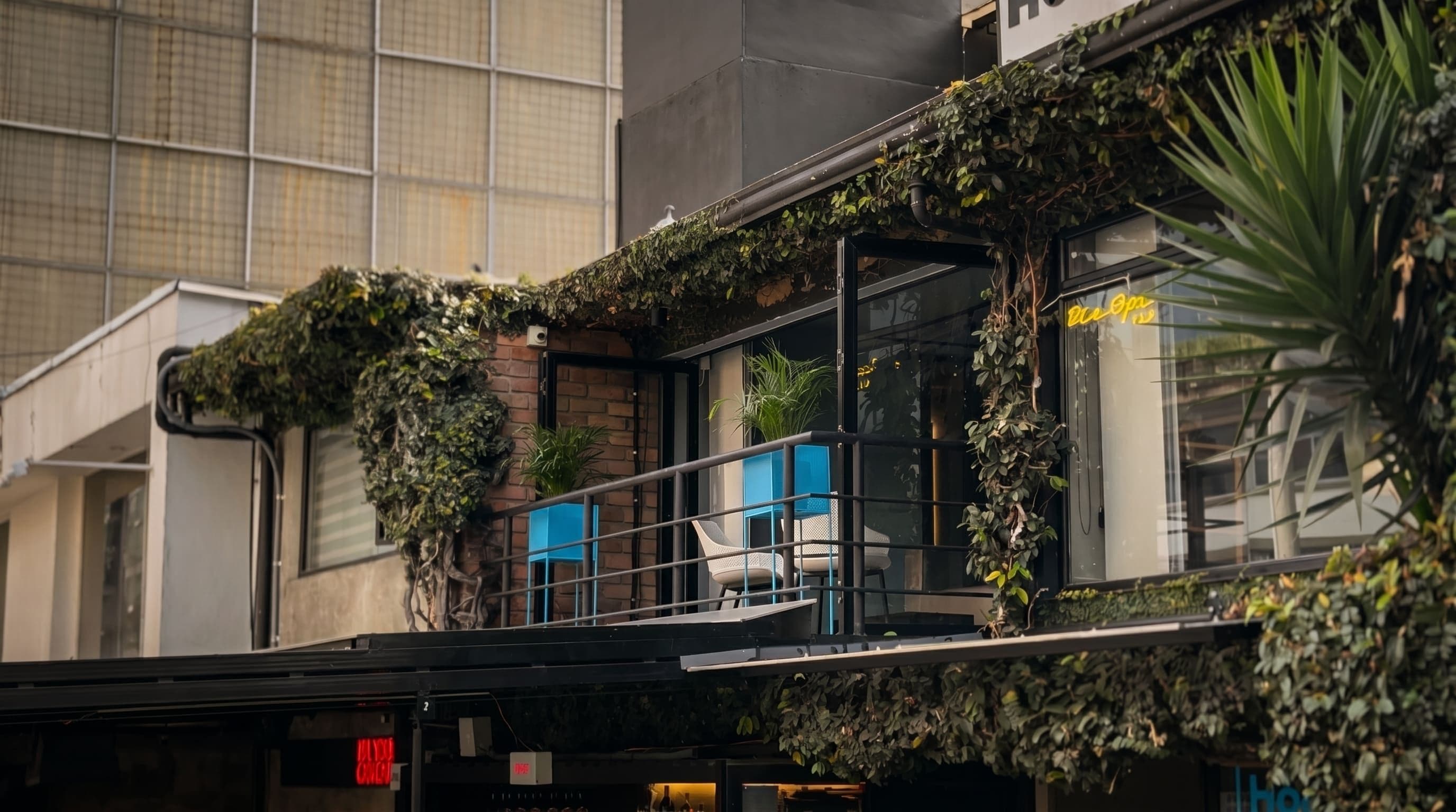Un edificio con balcón, un letrero con borde amarillo y un ventanal con reflejo.