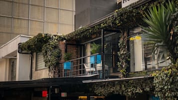 Un edificio con balcón, un letrero con borde amarillo y un ventanal con reflejo.
