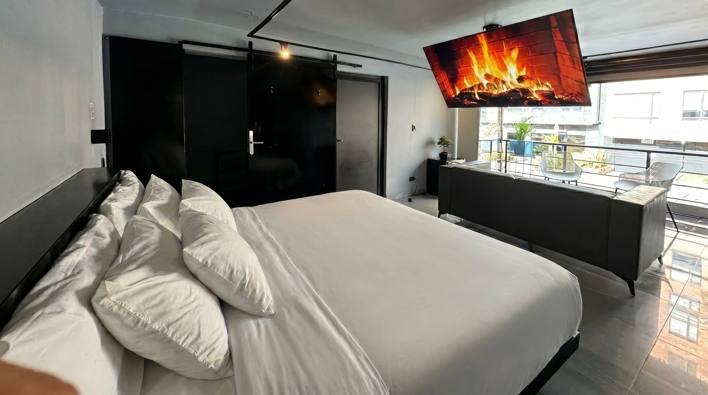 Un dormitorio moderno con una cama, un televisor montado en la pared y un balcón con vistas.