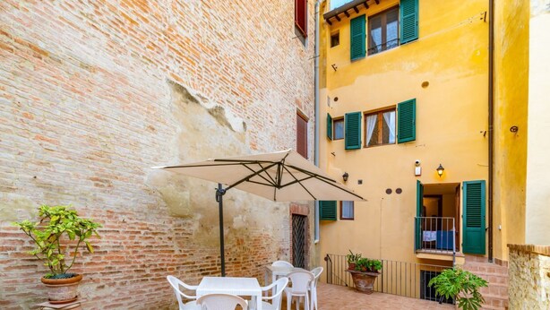 A courtyard with a brick wall, a yellow building with green shutters, outdoor furniture, and potted plants. - GuestHost - Beautiful studio of 25 square meters located on the first floor of a building without elevator (6 steps to access), can comfortably accommodate up to 2 people.The property is located in the historic center (Restricted Traffic Zone), just outs (Siensa)