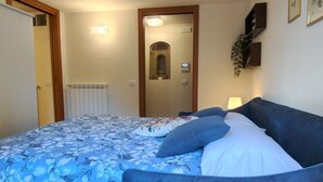 A bedroom with a bed, a radiator, a door, a mirror, and a wall-mounted shelf with a plant. - GuestHost - Beautiful studio of 25 square meters located on the first floor of a building without elevator (6 steps to access), can comfortably accommodate up to 2 people.The property is located in the historic center (Restricted Traffic Zone), just outs (Siensa)