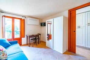 Ein Zimmer mit einer Couch, einem Esstisch mit Stühlen, einem Fernseher und einem Kleiderschrank.