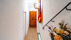 A hallway with a wooden door at the end, a flag on the wall, and a staircase with a handrail. - GuestHost - Beautiful studio of 25 square meters located on the first floor of a building without elevator (6 steps to access), can comfortably accommodate up to 2 people.The property is located in the historic center (Restricted Traffic Zone), just outs (Siensa)