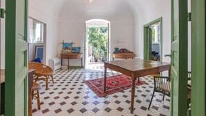 Una habitación con piso a cuadros, una mesa de madera, sillas de mimbre, un tapete rojo y un cuadro sobre un atril.