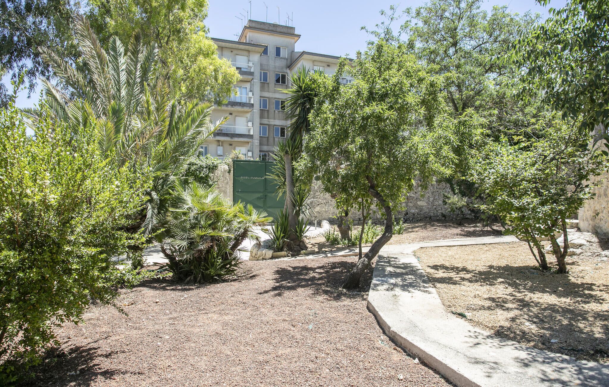 Une cour avec un sol en gravier, des arbres et un bâtiment en arrière-plan.