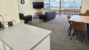 Un salon moderne doté d’un téléviseur à écran plat, d’un canapé en cuir noir et d’un coin repas avec une table en bois et des chaises marron.