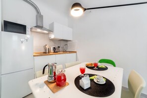 A modern kitchen with a white table set for breakfast, including a pitcher of red drink, a coffee cup, and a plate of pastries.