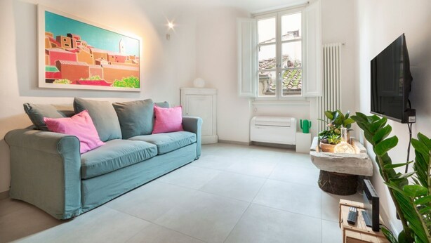 A living room with a sofa, a painting, a window, a radiator, and a television. - Casa San Martino in the feel of the middle age (Firenze)
