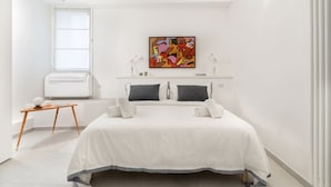 A bedroom with a bed, bedside lamps, a window with blinds, an air conditioner, and a small table with a lamp. - Casa San Martino in the feel of the middle age (Firenze)