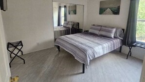 Una camera da letto con un letto, una ventola a soffitto, una finestra con tende, uno specchio e un piccolo tavolo.