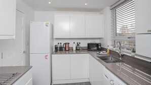 Een moderne keuken met witte kastjes, een RVS spoelbak en een magnetron.
