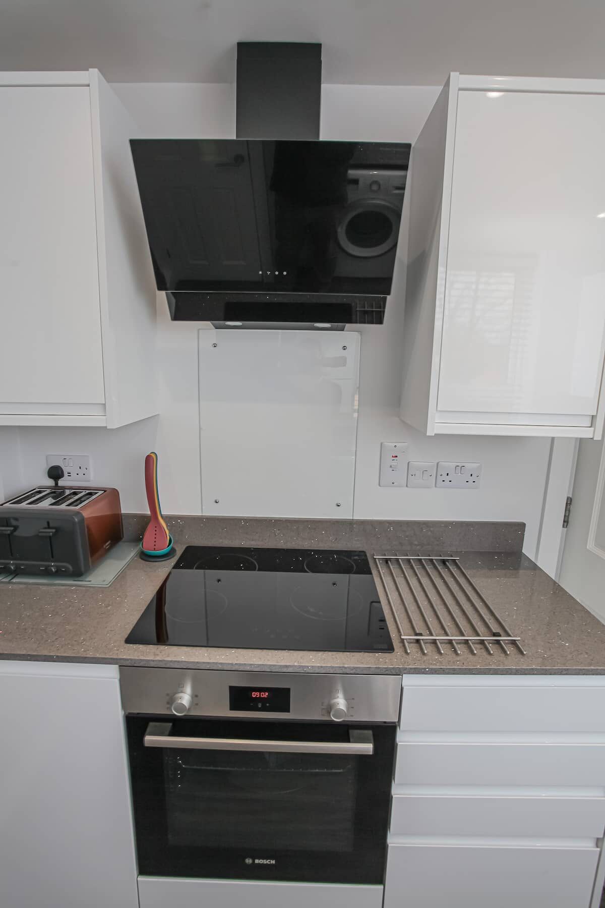 Une cuisine moderne équipée d’un four Bosch, d’une plaque de cuisson intégrée et d’une hotte noire.