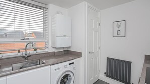 Een kleine keuken met een ingebouwde wasmachine, een spoelbak en een raam met zonwering.