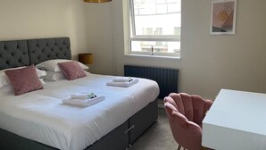 Hotelkamer met een groot bed, nachtkastje, stoel, raam met uitzicht en een kunstwerk aan de muur.