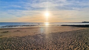 A beach with a clear sky and the sun setting over the horizon.