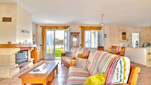 A cozy living room with a sofa, a wooden coffee table, and a fireplace. There is a kitchen area with a microwave and a sink.