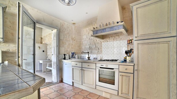 A kitchen with a stone wall backsplash, white cabinetry, a gas stove, and a coffee maker.