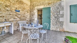 A stone-walled outdoor dining area with a table and chairs, a sink, and a view into the kitchen.