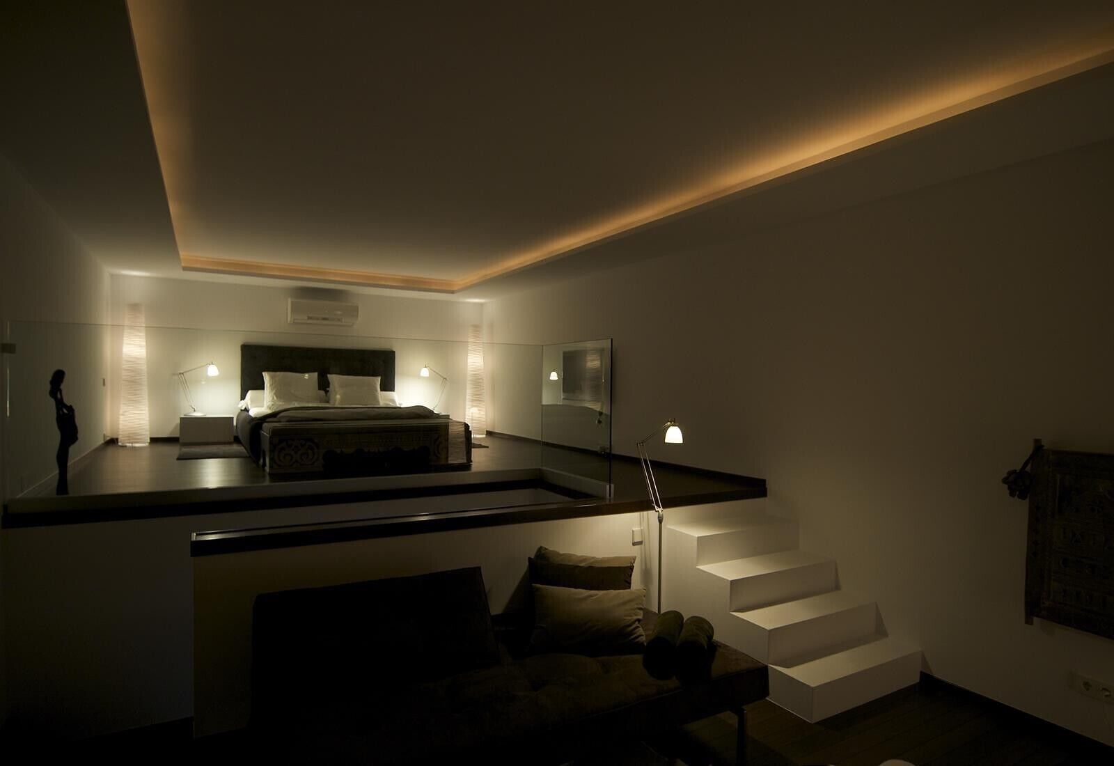 Een moderne slaapkamer met een bed, nachtkastjes, een bureau en een trap.