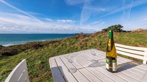 Une table avec une bouteille et des verres, donnant sur un paysage côtier.