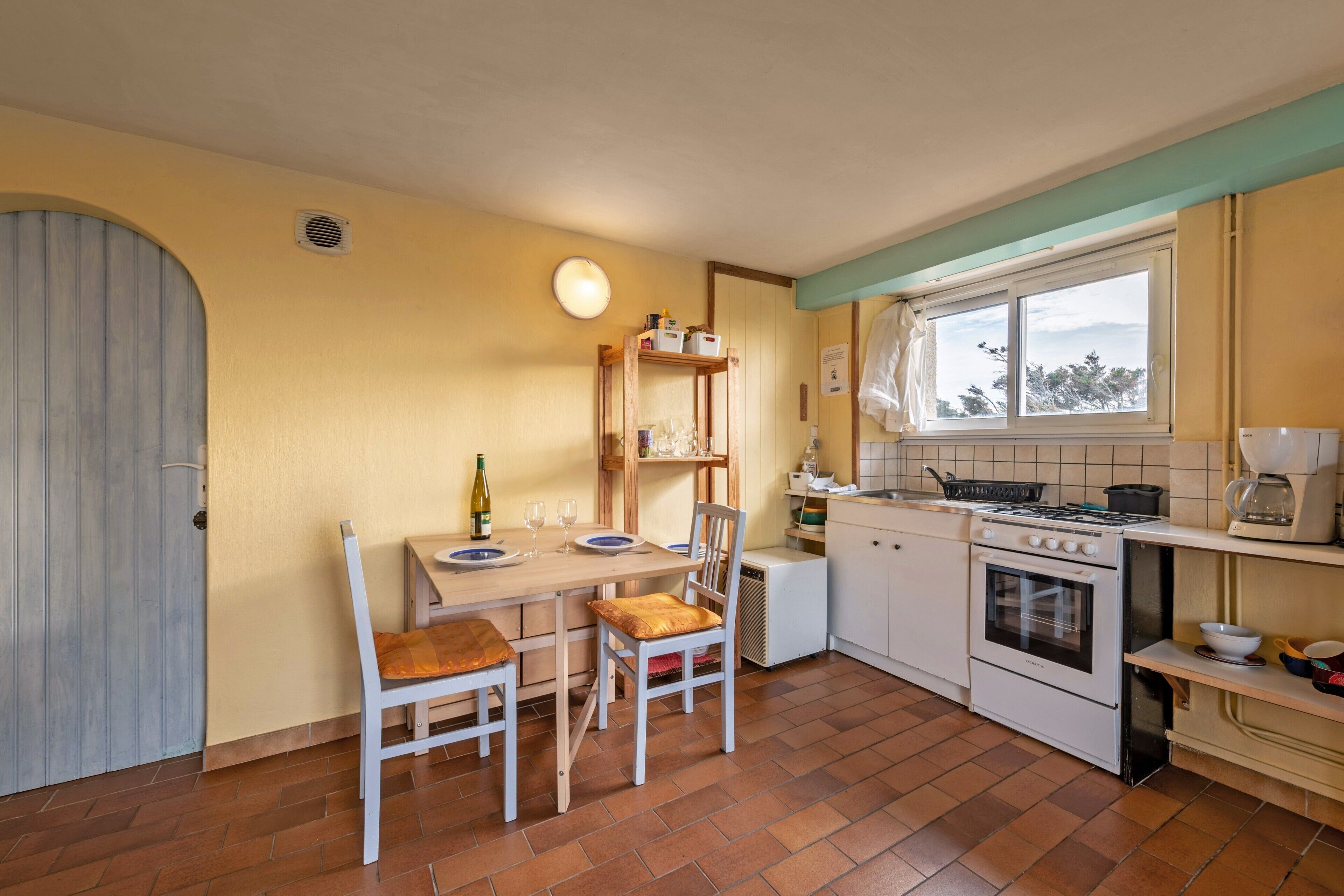 Een kleine keuken met een eettafel, stoelen, een fornuis en een raam.
