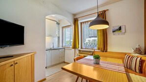 Kompakti keittiö, jossa on televisio, puukalusteet, ruokailutila pöytineen ja tuoleineen sekä ikkuna, jossa on verhot.