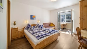 A bedroom with a wooden bed, bedside tables, a small seating area with a cushion, a window, and a view of the outside. - Studio Apartment 'Apartment Typ C Haus Pöder' with Mountain View (Naturno)