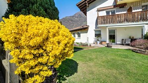 A two-story building with a balcony, a well-maintained lawn, and a mountain in the background. - Studio Apartment 'Apartment Typ C Haus Pöder' with Mountain View (Naturno)