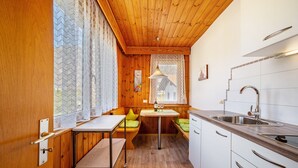 A compact kitchen with wooden walls, a built-in bench, a sink, and a window with lace curtains. - Apartment 'Typ B Haus Pöder' with Mountain View, Shared Garden and Wi-Fi (Naturno)