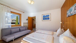 A room with a sofa, two beds, a window with curtains, a painting, and a door leading to another room. - Apartment 'Typ B Haus Pöder' with Mountain View, Shared Garden and Wi-Fi (Naturno)