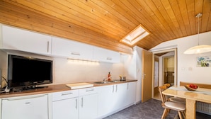 A modern kitchen with white cabinets, a built-in oven, a television, and a dining area with a wooden table and chairs. - Apartment 'Typ A Pöder's Haus' with Mountain View, Shared Garden and Wi-Fi (Naturno)