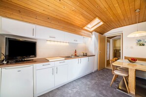 A modern kitchen with white cabinets, a built-in oven, a television, and a dining area with a wooden table and chairs.