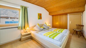 A bedroom with a wooden ceiling, a window with a view of a mountain, a bed with striped bedding, and a chair. - Apartment 'Typ A Pöder's Haus' with Mountain View, Shared Garden and Wi-Fi (Naturno)